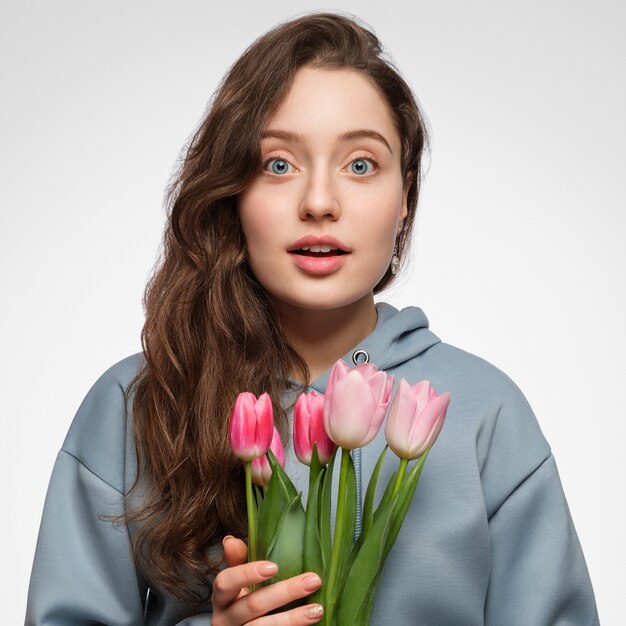 Mujer joven con tulipanes. Ojos azules, cabello largo y sorpresa en su rostro.