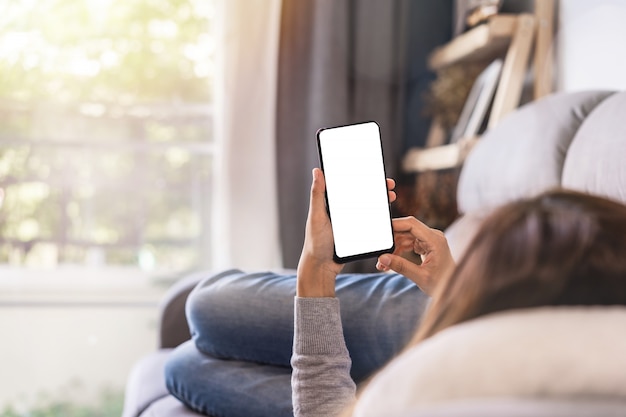 Mujer joven tumbado en el sofá en la sala de estar y utilizando el teléfono celular en casa