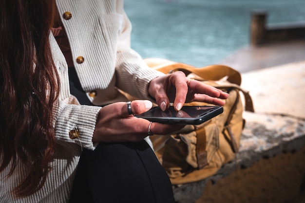 Mujer joven turista caucásica con el teléfono inteligente se sentó en un banco junto al mar.