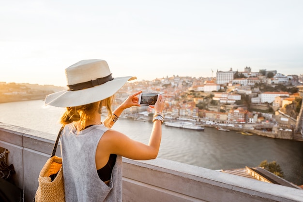 Mujer joven turista fotografiando con teléfono hermosa vista del paisaje en el casco antiguo con el río y el famoso puente de hierro en la ciudad de Oporto, Portugal