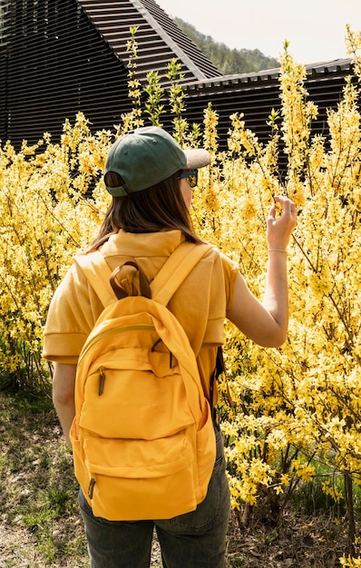 Mujer joven turista con mochila amarilla entre arbustos de forsythia florecientes tocando rama en primavera