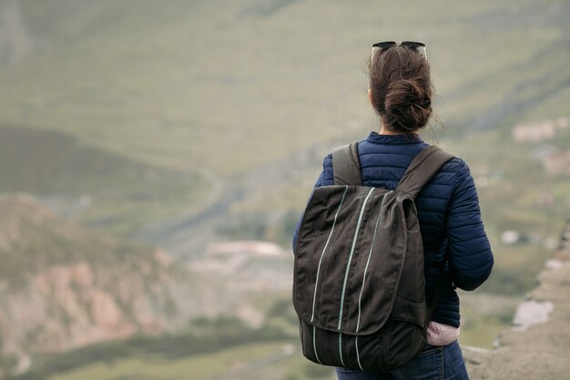 Mujer joven turista con mochila con el telón de fondo de las montañas del Cáucaso, Georgia en un día brumoso. vista trasera