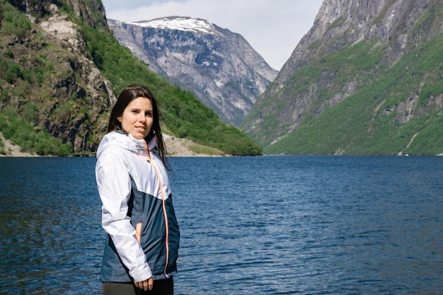 Mujer joven turista en primer plano y detrás de ella el fiordo con las altas montañas en Gudvangen Noruega