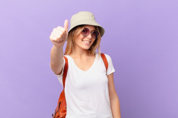 Mujer joven turista que se siente orgullosa, sonriendo positivamente con los pulgares hacia arriba