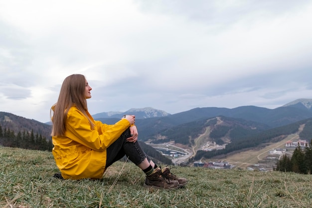 Mujer joven turista se sienta en la ladera con una taza en otoño Mujer viajera mira las montañas