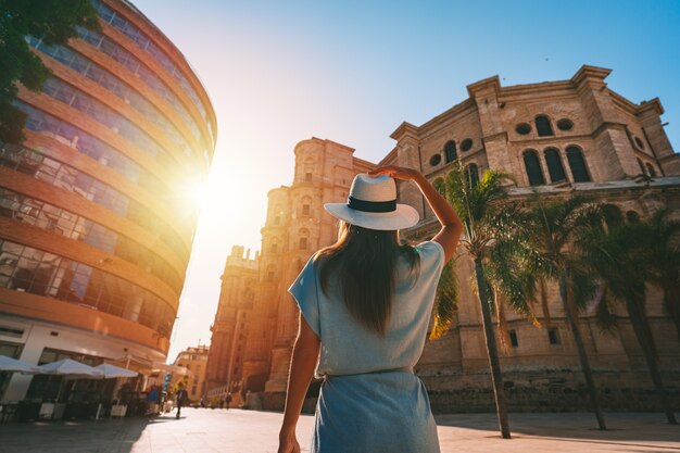 Foto mujer joven turista con sombrero blanco para el sol caminando en la ciudad de málaga al atardecer vacaciones en españa