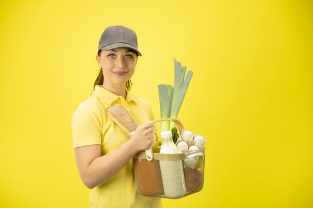 Mujer joven en uniforme amarillo manipulación cesta de alimentos, frutas, verduras, leche y huevos