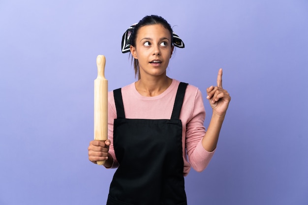 Mujer joven en uniforme de chef pensando en una idea apuntando con el dedo hacia arriba