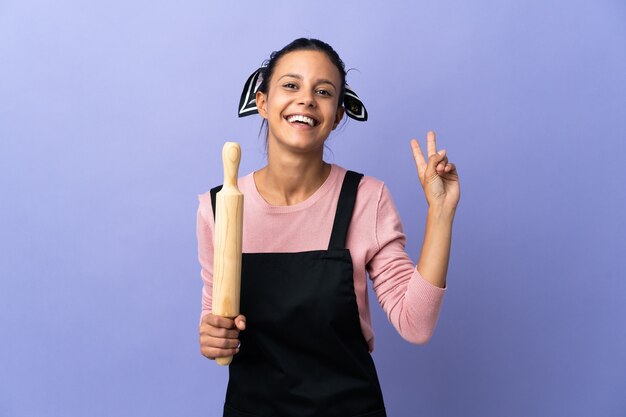 Mujer joven en uniforme de chef sonriendo y mostrando el signo de la victoria