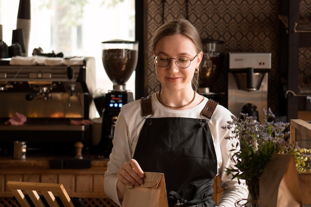 mujer joven en uniforme vendedora sosteniendo una bolsa de embalaje de papel artesanal para que la comida vaya a la cafetería o