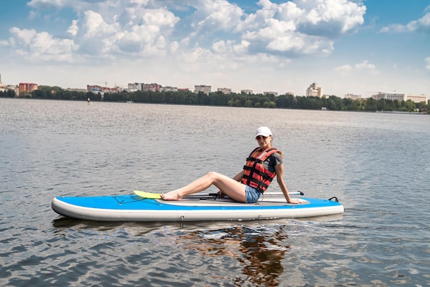 Una mujer joven usa chaleco salvavidas para remar en un hermoso lago en un día caluroso de verano, deporte de estilo de vida activo y relajación