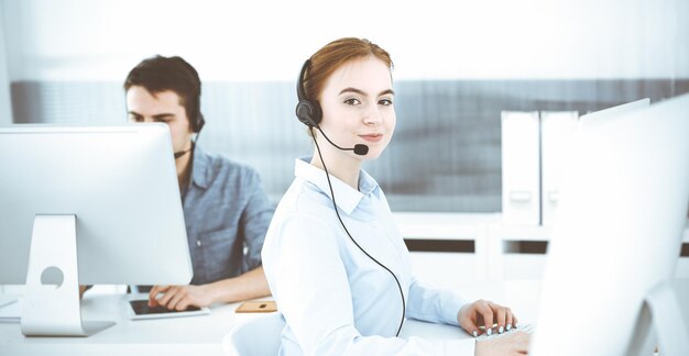 Mujer joven usando auriculares y computadora mientras habla con clientes en línea