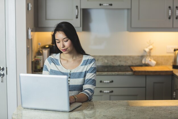 Mujer joven usando una computadora portátil en la cocina