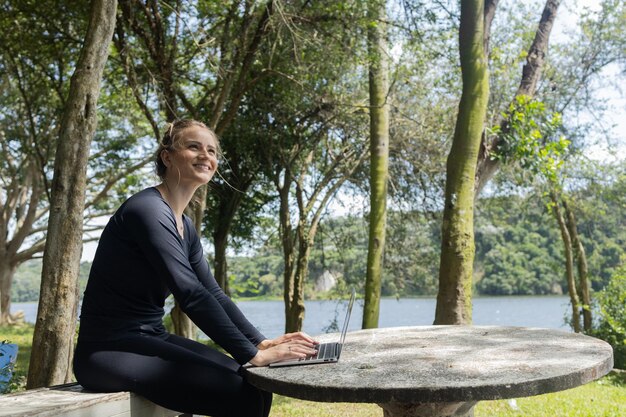 Foto mujer joven usando una computadora portátil durante el día en una tecnología de teléfono móvil en un parque verde