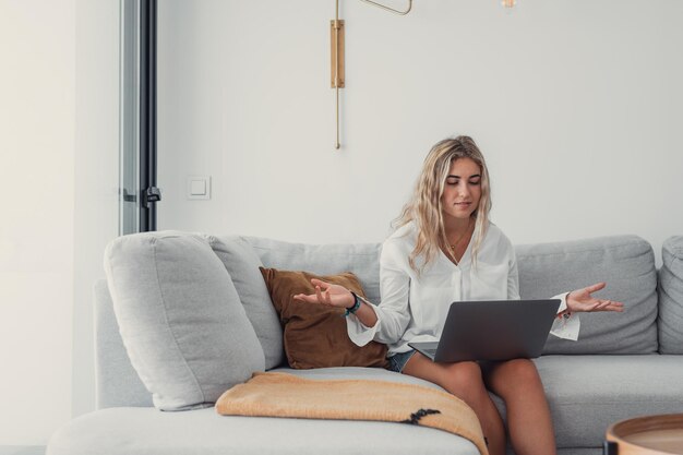 Mujer joven usando una computadora portátil mientras está sentada en el sofá en casa
