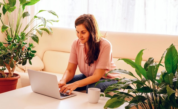 Mujer joven usando una computadora portátil mientras está sentada en el sofá en casa