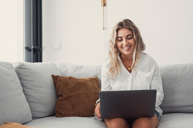 Mujer joven usando una computadora portátil mientras está sentada en el sofá en casa