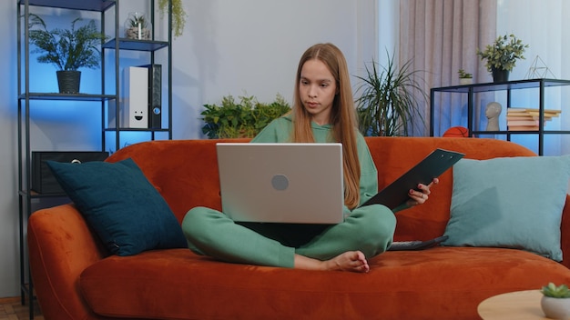 Mujer joven usando una computadora portátil mientras está sentada en el sofá en casa