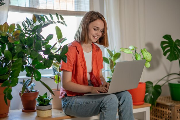 Mujer joven usando una computadora portátil mientras está sentada en el sofá en casa