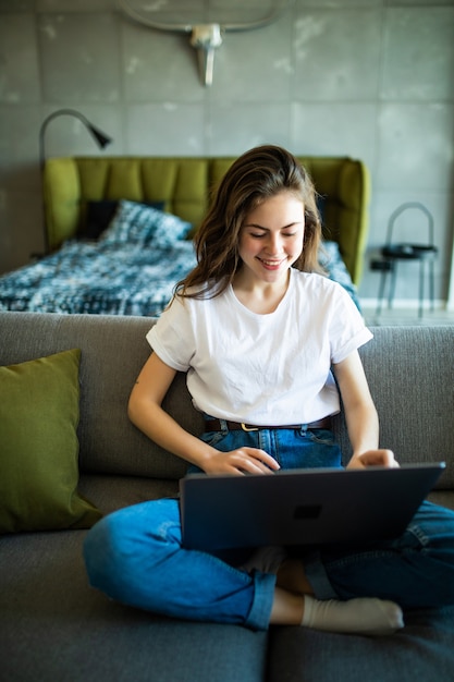 Mujer joven usando una computadora portátil mientras se relaja en el sofá