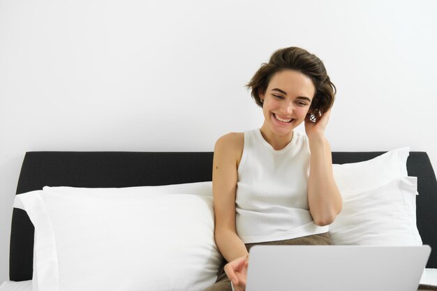 Foto mujer joven usando una computadora portátil mientras está sentada en la cama contra un fondo blanco