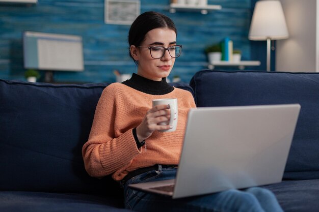 Foto mujer joven usando computadora portátil mientras está sentada en el sofá en casa.