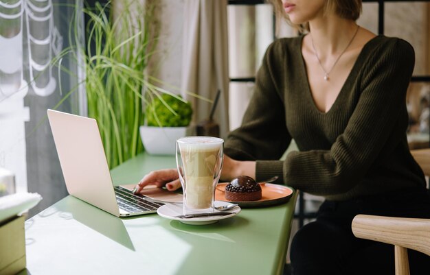 Mujer joven usando laptop con postre y taza de café en la cafetería