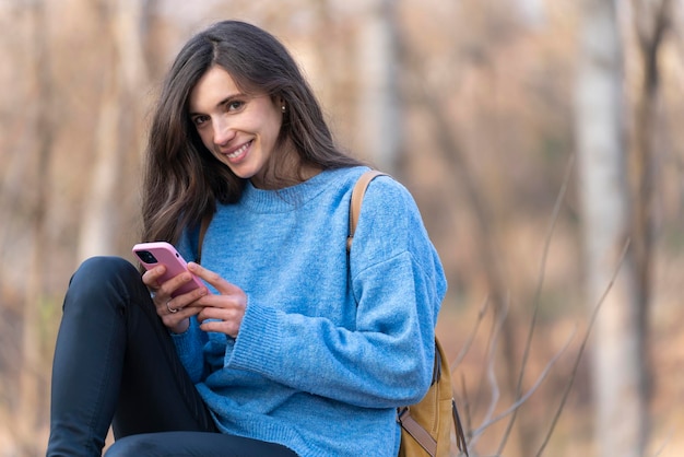 Mujer joven usando su teléfono inteligente y mirando a la cámara y sonriendo