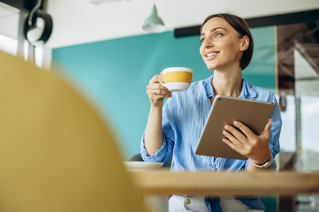 Mujer joven usando tableta en un café y bebiendo café