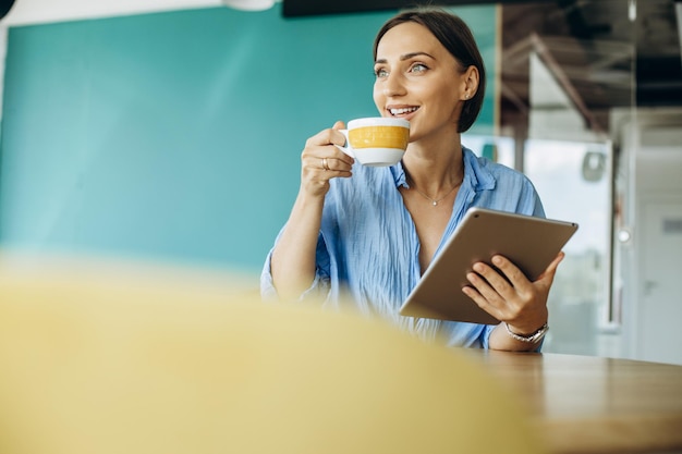 Mujer joven usando tableta en un café y bebiendo café