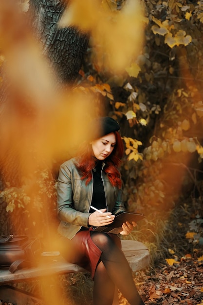 Mujer joven usando una tableta digital mientras está sentada cerca de un árbol