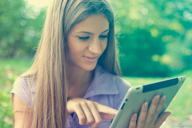 Mujer joven usando una tableta digital mientras está sentada en el parque