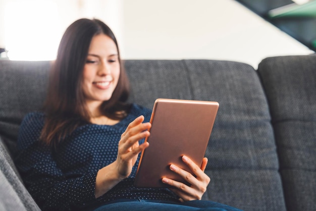 Foto mujer joven usando una tableta digital mientras está sentada en el sofá en casa