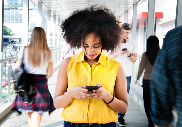 Foto mujer joven usando un teléfono inteligente en medio de la multitud caminando