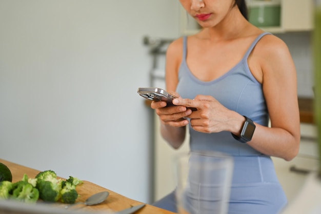 Mujer joven usando un teléfono inteligente mientras prepara un desayuno saludable vegano en la cocina