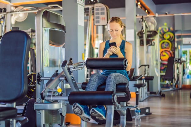 Mujer joven usando el teléfono mientras entrena en el gimnasio