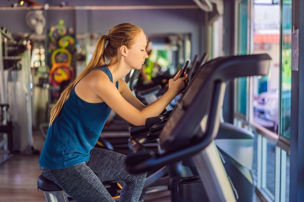 Mujer joven usando el teléfono mientras entrena en el gimnasio