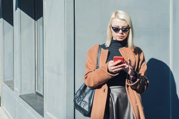 Mujer joven usando el teléfono mientras está de pie contra la pared