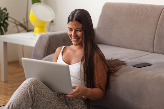 Mujer joven usando el teléfono mientras está sentada en el sofá en casa