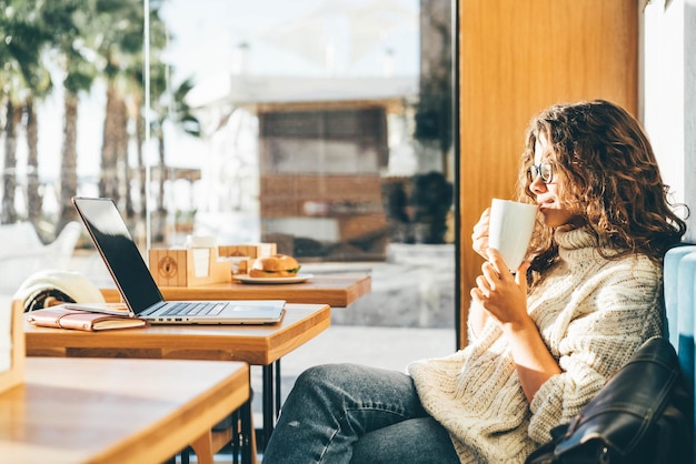 Mujer joven usando teléfono móvil mientras está sentada en una cafetería