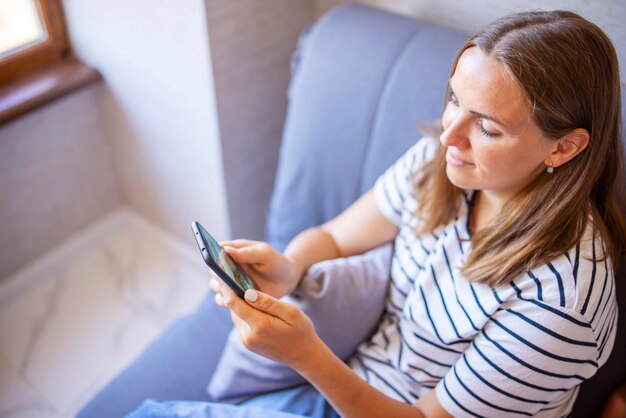 Mujer joven usando teléfono móvil mientras está sentada en casa