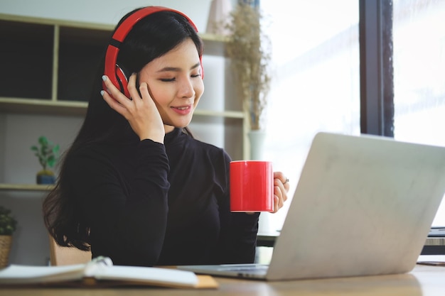 Mujer joven usando teléfono móvil mientras está sentada en una computadora portátil