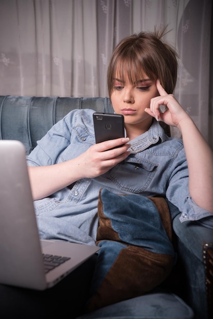 Mujer joven usando teléfono móvil mientras está sentada en el sofá en casa