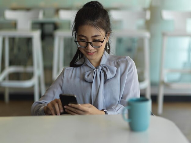 Foto mujer joven usando teléfono móvil mientras está sentada en la mesa