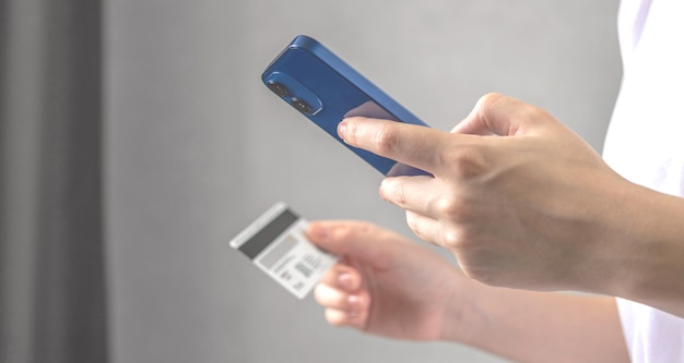 Mujer joven utiliza el teléfono móvil para realizar pedidos en línea y pagar facturas con tarjeta de crédito en el interior de la sala de estar en casa. Smartphone y tarjeta de crédito en primer plano de la mano, foto de banner