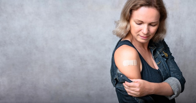 Mujer joven vacunada que muestra el brazo con yeso en el fondo de la pared gris