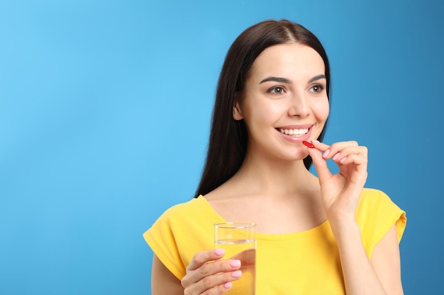 Mujer joven con vaso de agua tomando cápsula de vitamina sobre fondo azul claro Espacio para texto