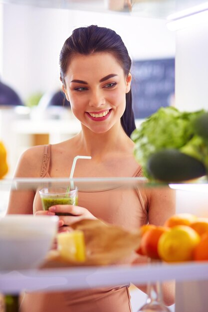 Mujer joven con un vaso de sabroso batido saludable en la mesa en la cocina