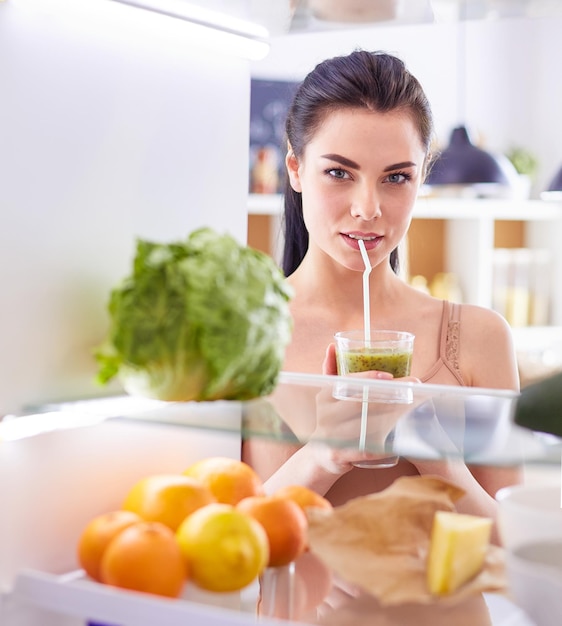 Mujer joven con un vaso de sabroso batido saludable en la mesa en la cocina