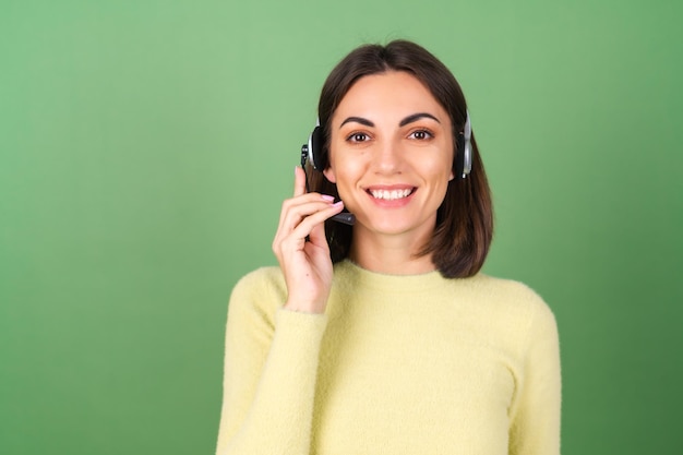 Mujer joven en verde en un suéter amarillo gerente, trabajador de servicio de apoyo, vendedor, acepta con placer llamadas de clientes